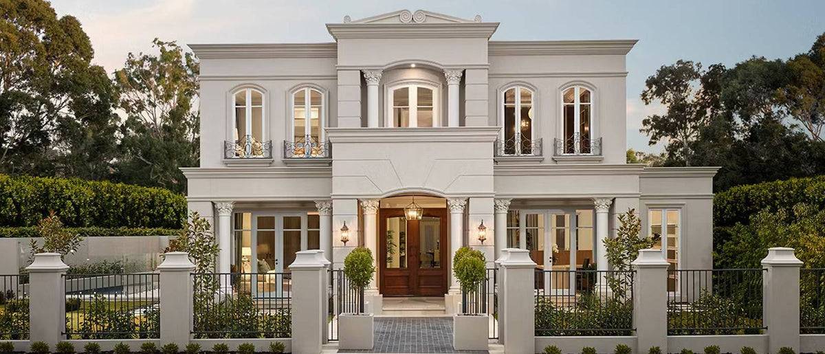 Residential luxury home featuring Mouldex composite exterior mouldings, including window headers, door surrounds, and roofline cornices in a natural limestone finish.