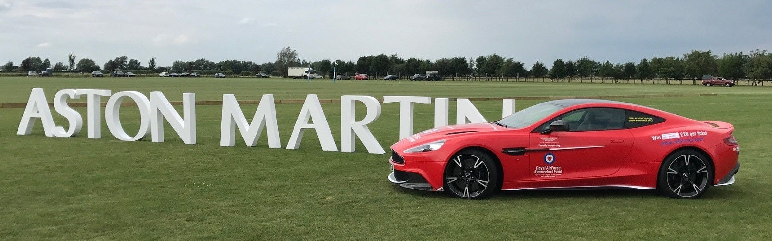 Large-scale "ASTON MARTIN" brand signage custom-cut from high-density foam, displayed at an outdoor event alongside a red Aston Martin sports car.
