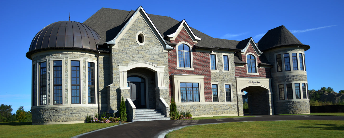 Extensive luxury estate exterior featuring a mix of stone and brickwork with custom cement-coated foam architectural details, including a grand arched entryway and a rounded turret with matching cornice mouldings.
